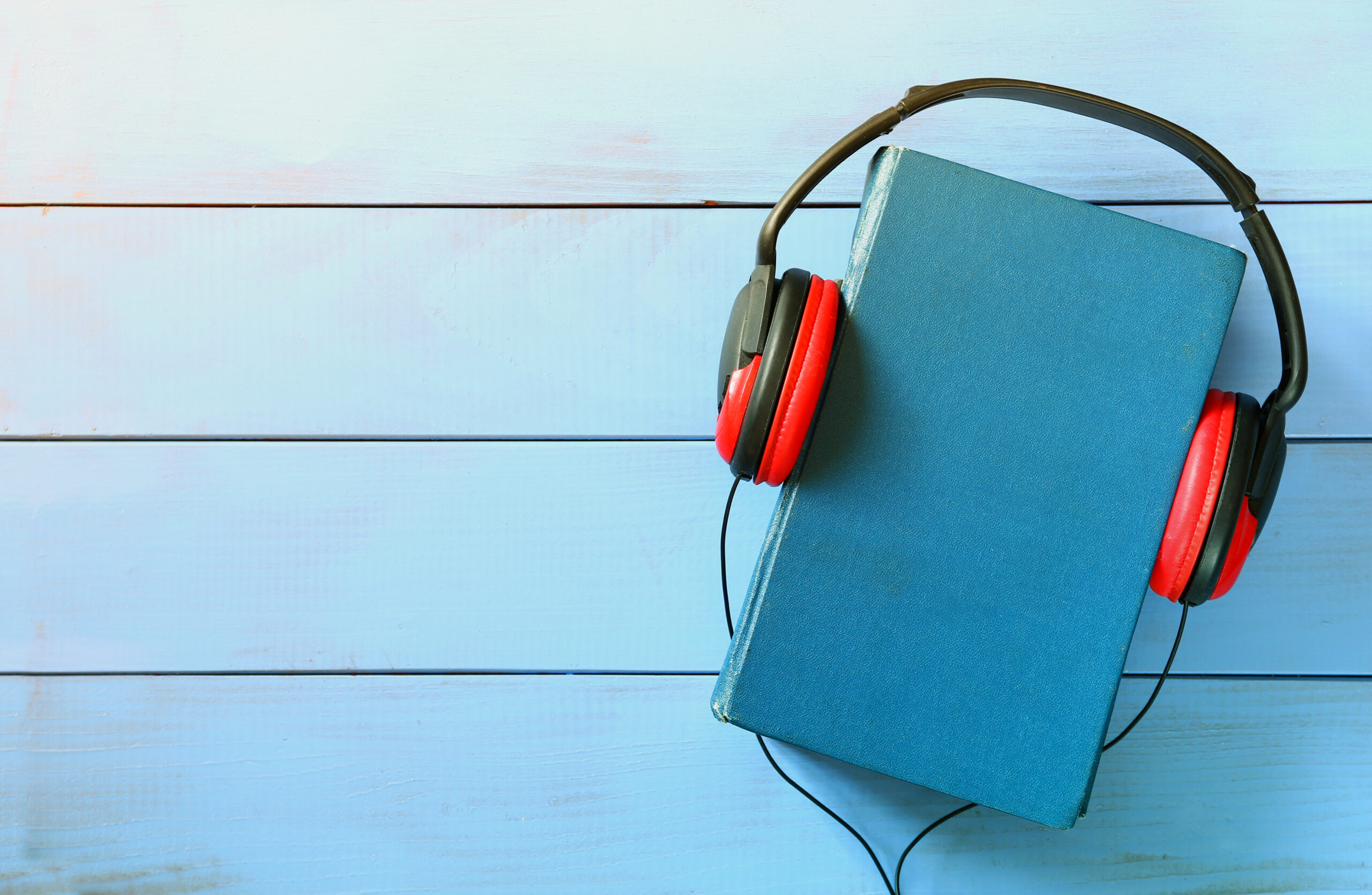 top view of audio book concept, blue cover book and headphones over wooden table