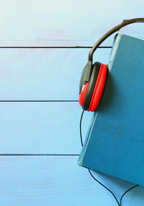 top view of audio book concept, blue cover book and headphones over wooden table