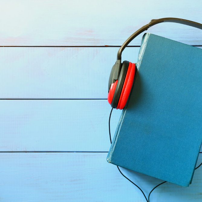 top view of audio book concept, blue cover book and headphones over wooden table